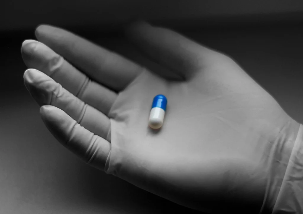 Gloved hand holding a single capsule pill, representing general medication information